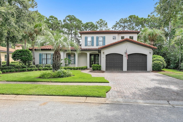 mediterranean / spanish-style house featuring decorative driveway, an attached garage, a front lawn, and stucco siding