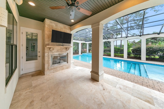 outdoor pool with glass enclosure, a patio, ceiling fan, and a tiled fireplace