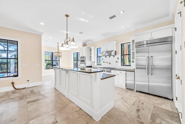 kitchen with visible vents, under cabinet range hood, dark countertops, built in fridge, and crown molding