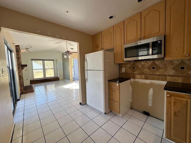 kitchen with light tile patterned floors, lofted ceiling, freestanding refrigerator, decorative backsplash, and stainless steel microwave