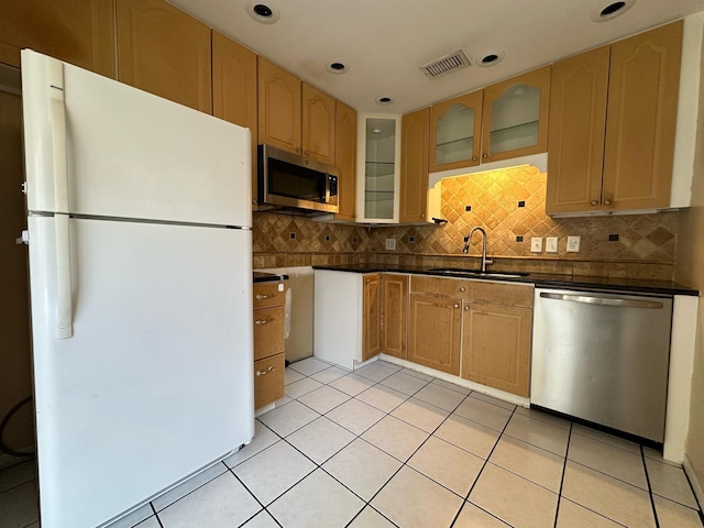 kitchen featuring a sink, tasteful backsplash, dark countertops, appliances with stainless steel finishes, and glass insert cabinets