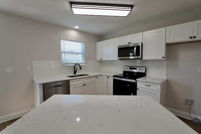 kitchen with light stone countertops, decorative backsplash, stainless steel appliances, white cabinetry, and a sink