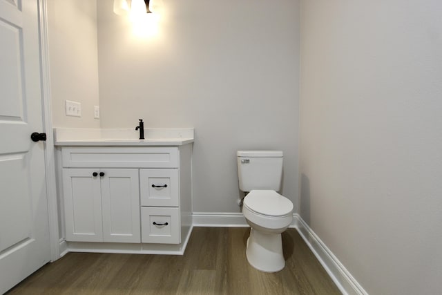 bathroom with toilet, vanity, baseboards, and wood finished floors