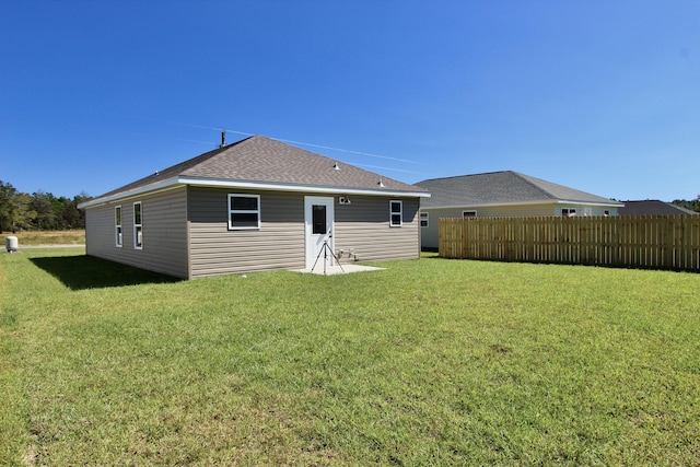 rear view of house featuring a yard, fence, and a shingled roof