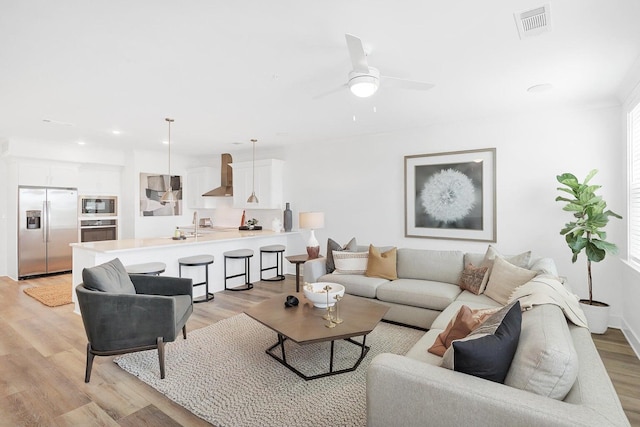 living area featuring visible vents, baseboards, light wood-type flooring, and a ceiling fan