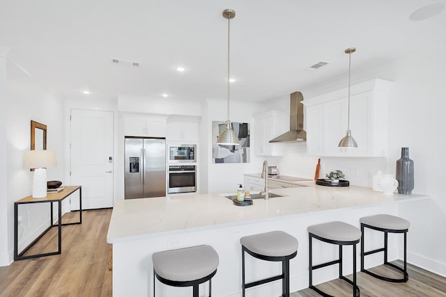 kitchen with a peninsula, a sink, decorative backsplash, appliances with stainless steel finishes, and wall chimney range hood