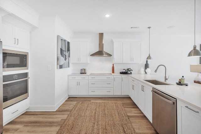 kitchen with a sink, stainless steel appliances, light wood-style floors, and wall chimney range hood