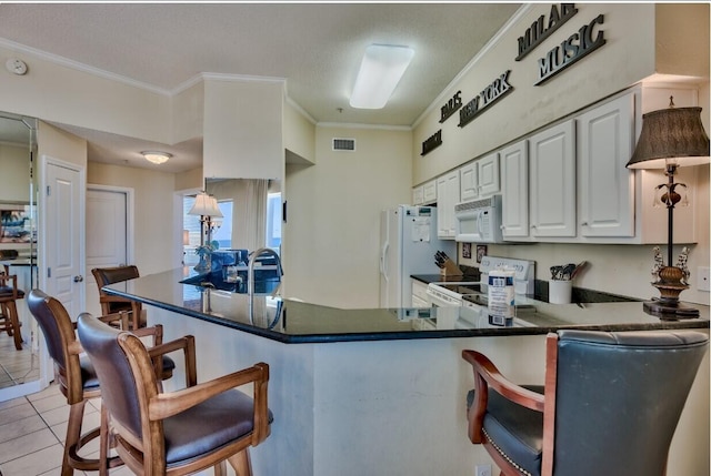 kitchen with light tile patterned floors, visible vents, white appliances, and a kitchen bar