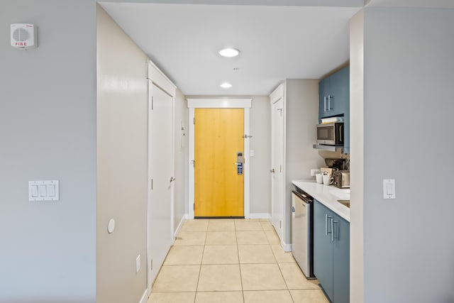 kitchen with dishwashing machine, light tile patterned flooring, light countertops, stainless steel microwave, and blue cabinets