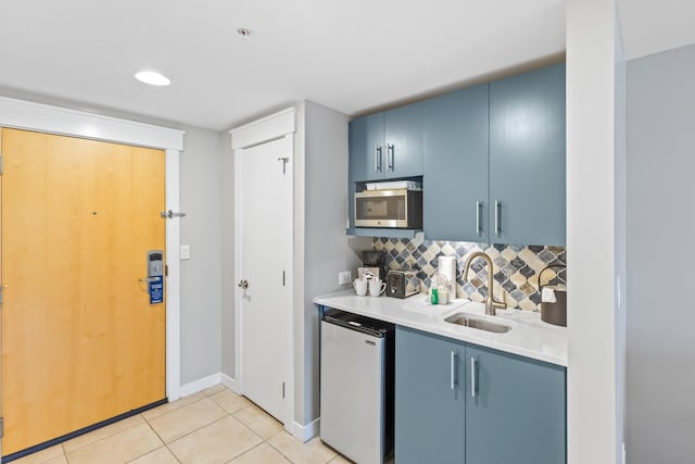 kitchen with fridge, blue cabinets, a sink, and stainless steel microwave