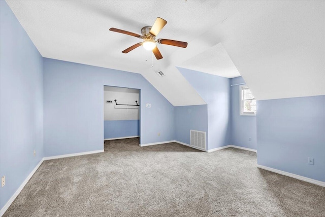 additional living space featuring visible vents, a textured ceiling, baseboards, ceiling fan, and vaulted ceiling