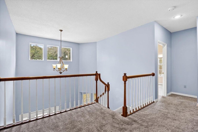 hall featuring baseboards, carpet floors, a textured ceiling, an upstairs landing, and a chandelier