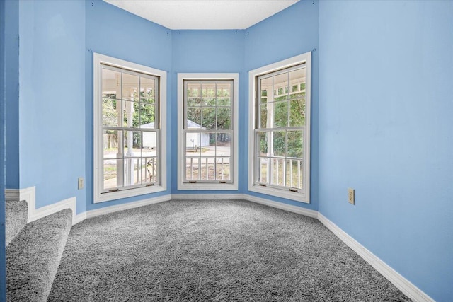 carpeted empty room featuring stairs and baseboards