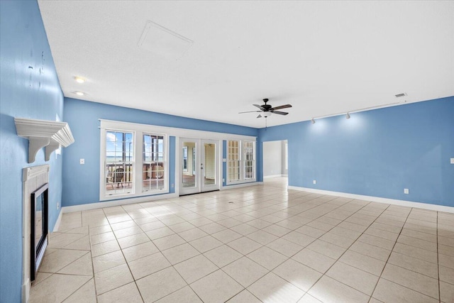 unfurnished living room featuring tile patterned flooring, ceiling fan, a tile fireplace, and baseboards