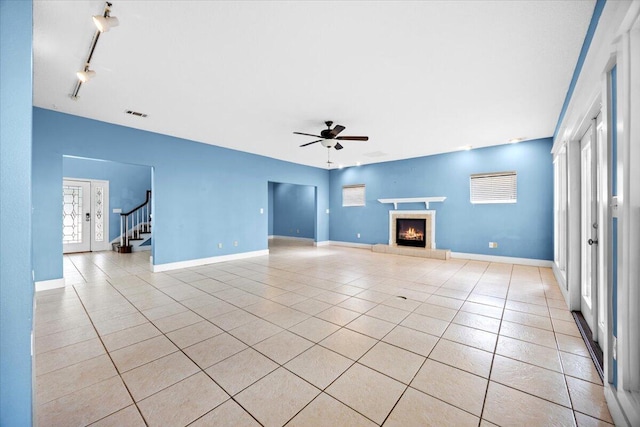 unfurnished living room featuring light tile patterned flooring, a tiled fireplace, baseboards, and ceiling fan