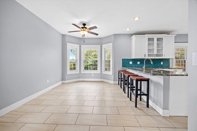 kitchen with tasteful backsplash, glass insert cabinets, ceiling fan, a kitchen bar, and white cabinets