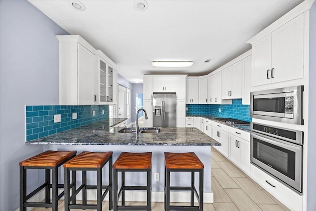 kitchen with a kitchen bar, a sink, stainless steel appliances, a peninsula, and glass insert cabinets