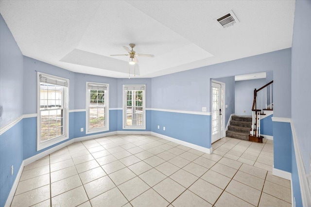 unfurnished room featuring visible vents, a ceiling fan, baseboards, light tile patterned flooring, and a raised ceiling