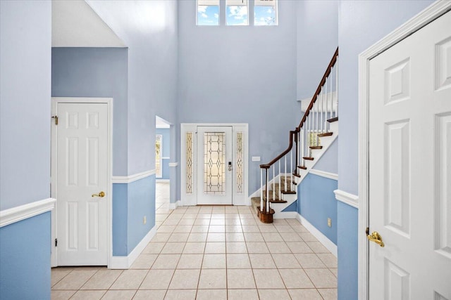 foyer featuring a towering ceiling, baseboards, light tile patterned flooring, and stairs