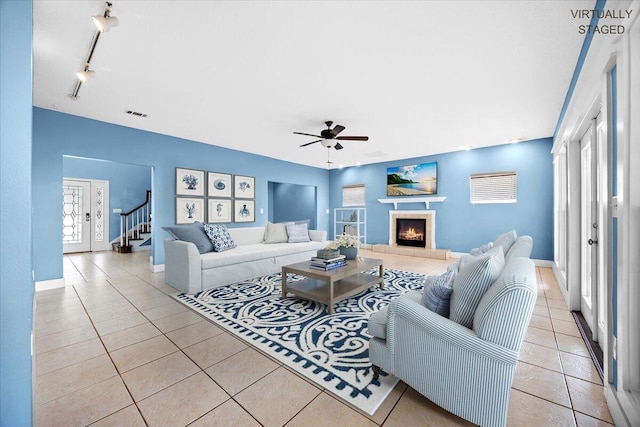 tiled living room featuring stairway, a ceiling fan, visible vents, a tile fireplace, and rail lighting