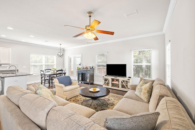 living room with wood finished floors, baseboards, visible vents, ceiling fan, and ornamental molding