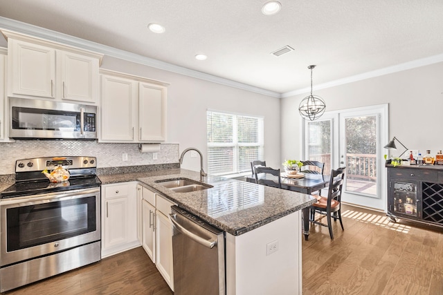 kitchen featuring visible vents, a peninsula, a sink, ornamental molding, and stainless steel appliances