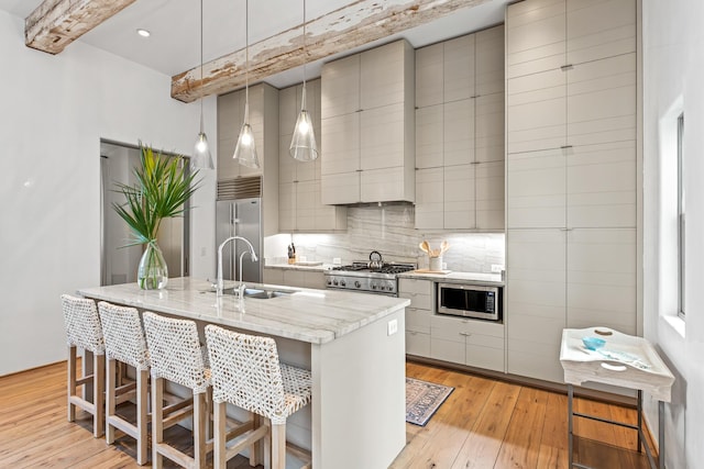 kitchen with light wood finished floors, a sink, built in appliances, modern cabinets, and backsplash