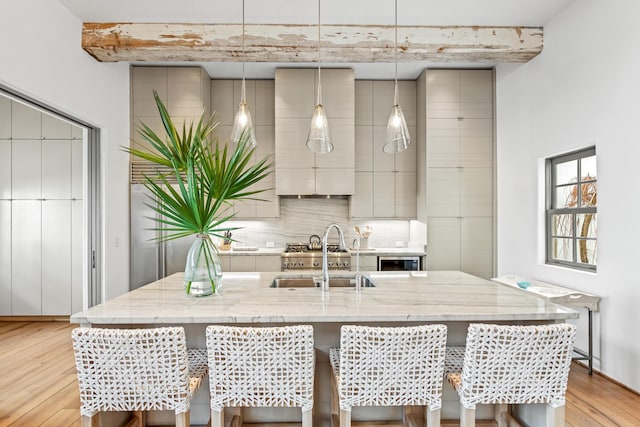 kitchen with light wood finished floors, backsplash, light stone countertops, a breakfast bar area, and a sink