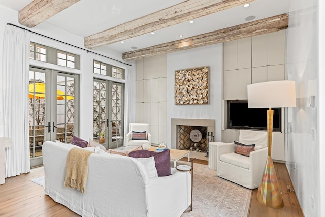 living room featuring light wood finished floors, beamed ceiling, a fireplace with flush hearth, recessed lighting, and french doors