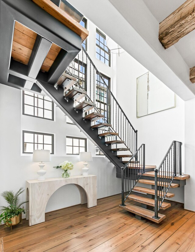 staircase with a wealth of natural light, beamed ceiling, wood-type flooring, and a towering ceiling