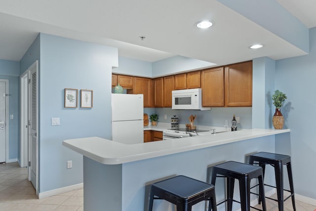 kitchen with a kitchen bar, light countertops, brown cabinets, a peninsula, and white appliances