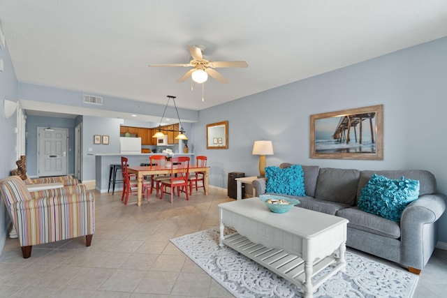 living area featuring light tile patterned floors, visible vents, baseboards, and a ceiling fan