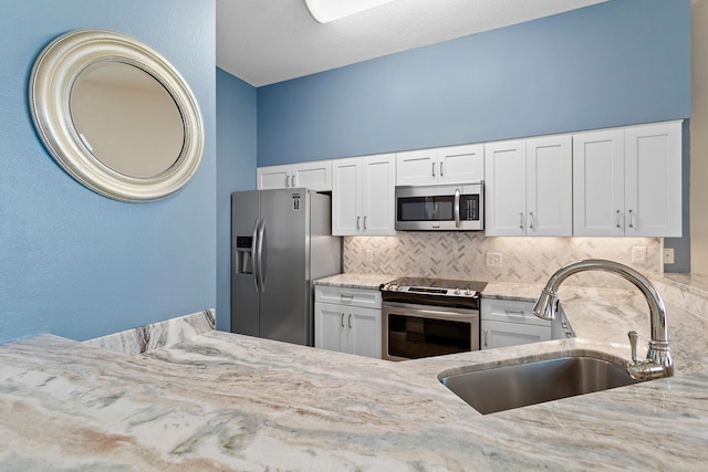 kitchen featuring light stone countertops, a sink, decorative backsplash, appliances with stainless steel finishes, and white cabinetry