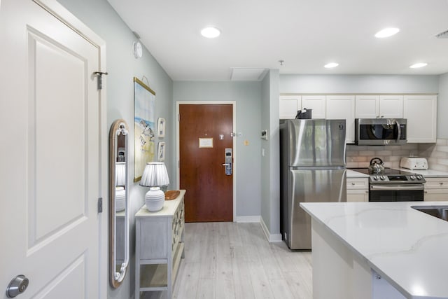 kitchen featuring tasteful backsplash, appliances with stainless steel finishes, white cabinets, light wood finished floors, and light stone countertops