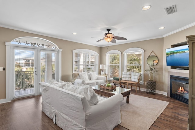 living room featuring dark wood-style floors, baseboards, visible vents, a fireplace, and ornamental molding