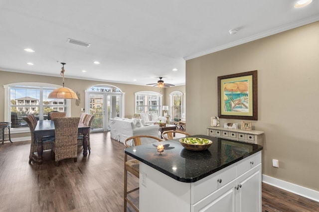 kitchen featuring dark wood-style floors, visible vents, baseboards, a breakfast bar, and crown molding