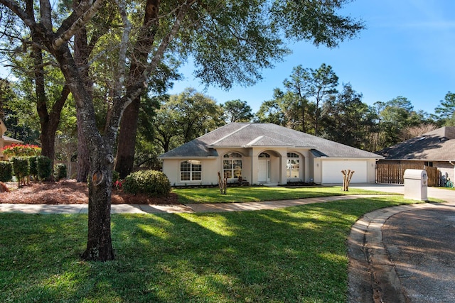 view of front facade with stucco siding, driveway, fence, a front yard, and a garage