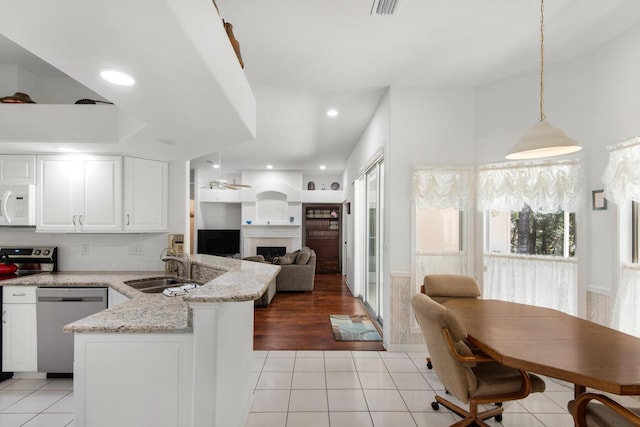 kitchen with a sink, appliances with stainless steel finishes, a peninsula, light tile patterned floors, and a tile fireplace