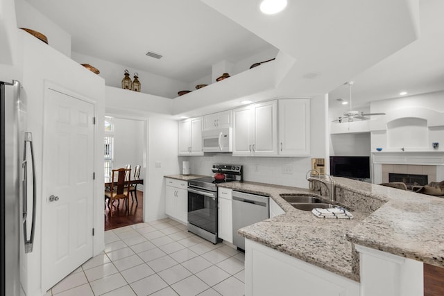 kitchen with a peninsula, a sink, stainless steel appliances, open floor plan, and backsplash