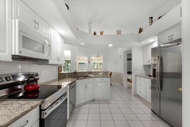 kitchen featuring light tile patterned floors, a peninsula, appliances with stainless steel finishes, white cabinetry, and a raised ceiling