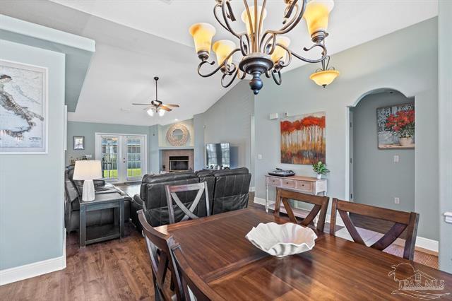 1607 Woodlawn Way, Gulf Breeze, FL 32563 - dining space featuring ceiling fan, a glass covered fireplace, arched walkways, wood finished floors, and a chandelier