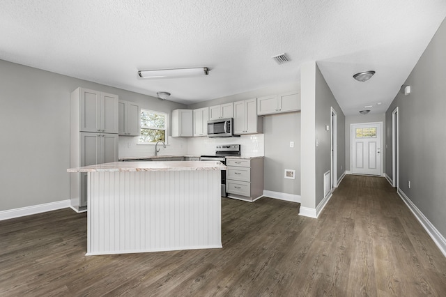 kitchen with a sink, a kitchen island, dark wood-style floors, stainless steel appliances, and baseboards