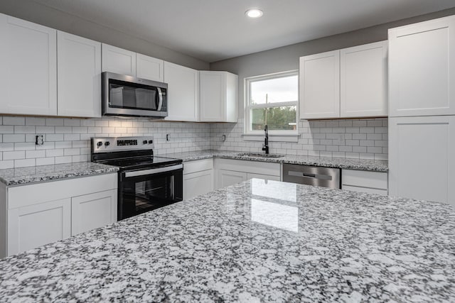 kitchen featuring a sink, white cabinetry, stainless steel appliances, decorative backsplash, and light stone countertops