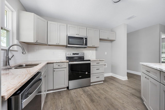 kitchen with light wood-style flooring, a sink, backsplash, appliances with stainless steel finishes, and light stone countertops