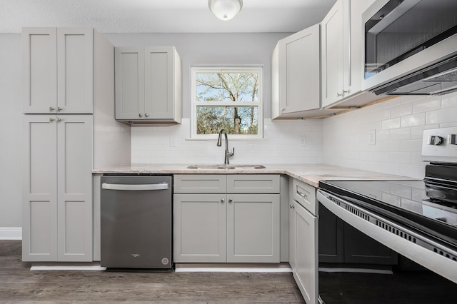 kitchen with a sink, tasteful backsplash, wood finished floors, appliances with stainless steel finishes, and light stone countertops