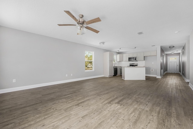 unfurnished living room with dark wood finished floors, visible vents, a ceiling fan, and baseboards