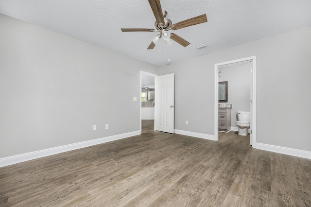 unfurnished bedroom with visible vents, ensuite bathroom, a textured ceiling, wood finished floors, and baseboards