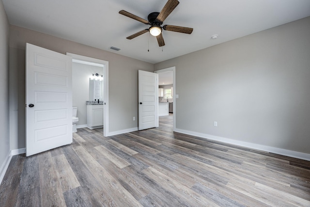 unfurnished bedroom featuring visible vents, connected bathroom, baseboards, wood finished floors, and a ceiling fan