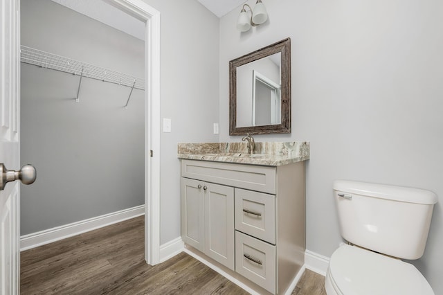 bathroom with vanity, wood finished floors, baseboards, a walk in closet, and toilet