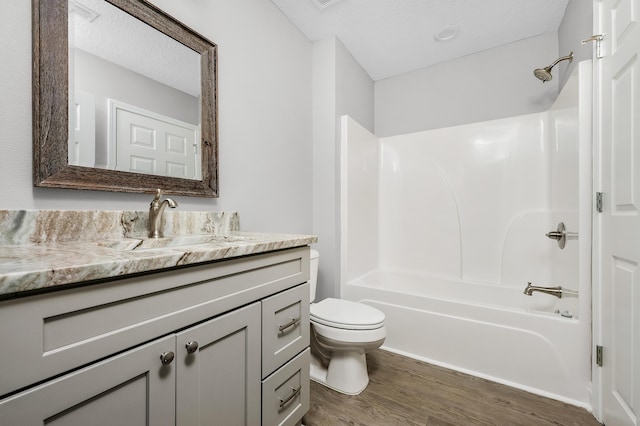 full bathroom with vanity, wood finished floors,  shower combination, a textured ceiling, and toilet